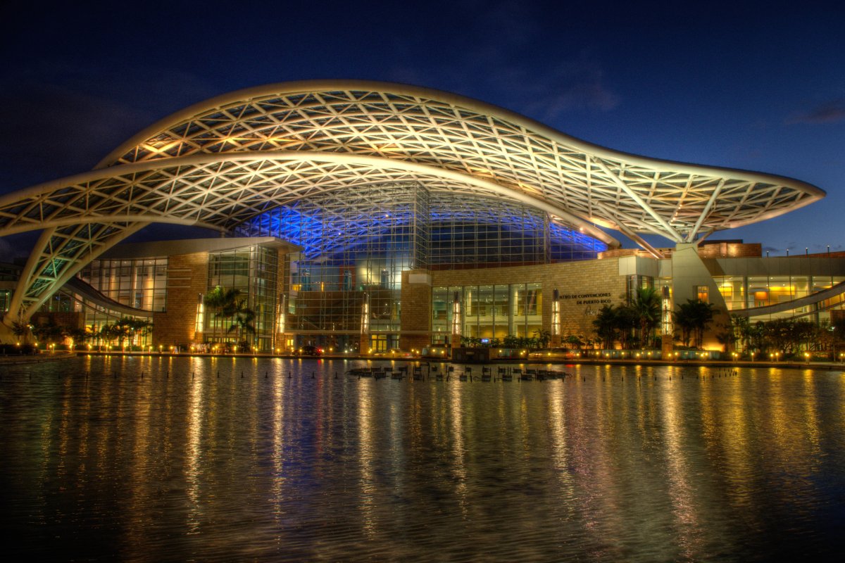 El exterior del Centro de Convenciones de Puerto Rico de noche, con luces reflejadas en el agua.