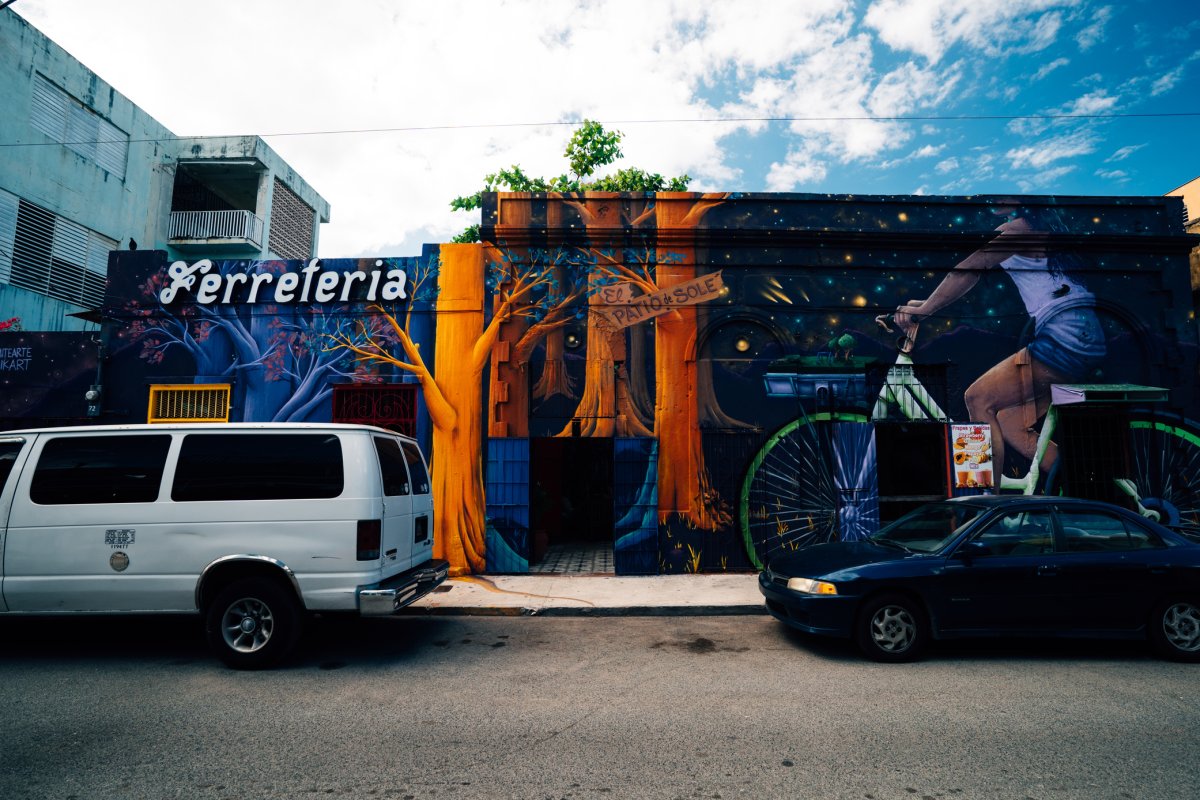 Autos estacionados a lo largo de una calle en el área de Santurce de San Juan con un colorido mural en el edificio
