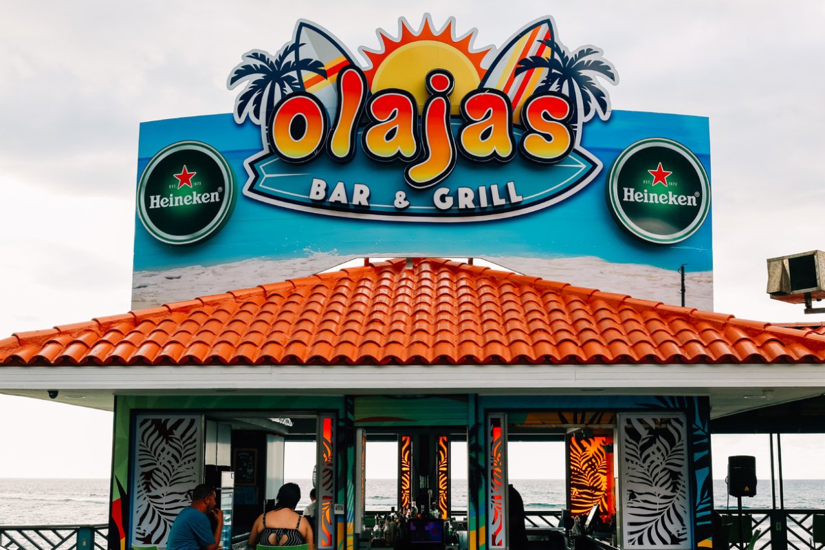 La colorida fachada de Olaja's Bar & Grill en Aguada con el océano al fondo