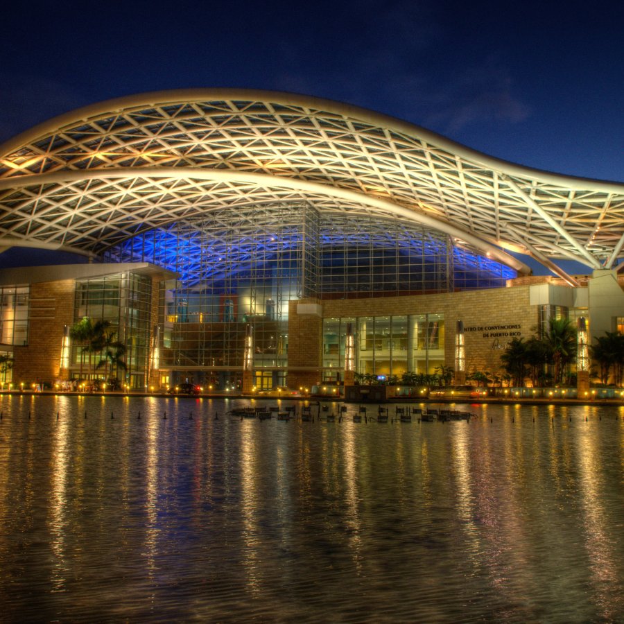 El exterior del Centro de Convenciones de Puerto Rico de noche, con luces reflejadas en el agua.
