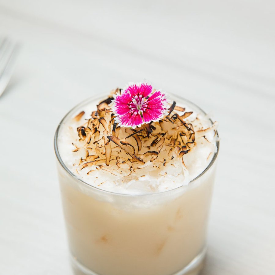 A rum cocktail, created by Chef Mario Pagan, is topped with toasted coconut and a pink flower.