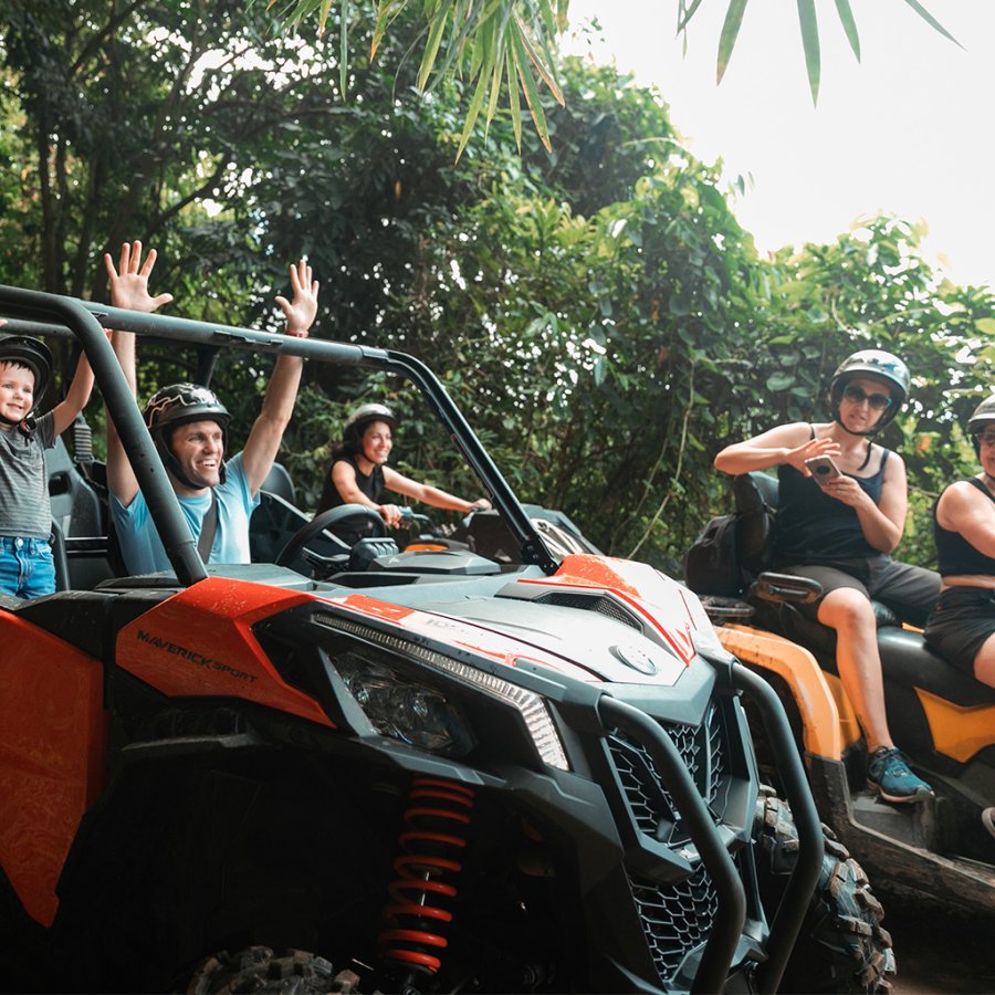 Man and son celebrating with their hands up inside an ATV going through the rainforest in Puerto Rico. The mother in another ATV and two other women on ATVs surround them.