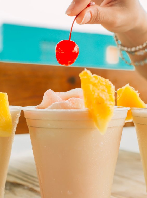 A frozen cocktail is garnished with maraschino cherries and fresh pineapple slices.