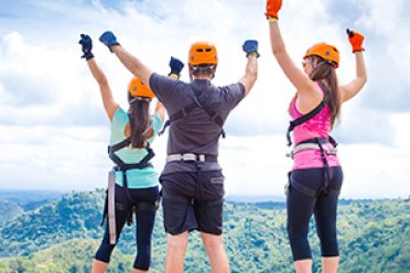 Three people with hands in the air wearing zipline gear.