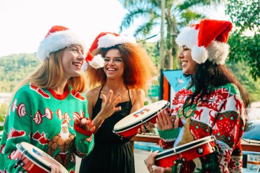 Three young ladies wearing Santa hats and Christmas sweaters playing the pandero, a typical instrument of Puerto Rico's Christmas parrandas.