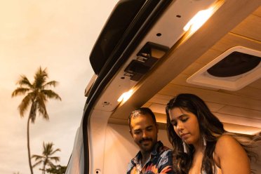 A couple works on tablets while sitting in the back of a van with the back open.