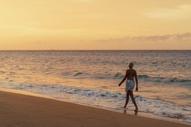 A woman walks along the shoreline at sunset, with gentle waves and golden light reflecting off the water on a peaceful Puerto Rican beach.