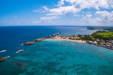 Aerial view of Playa Puerto Nuevo in Vega Baja, Puerto Rico, showing turquoise waters, rocky natural breakwaters, and a sandy beach along the north coast.