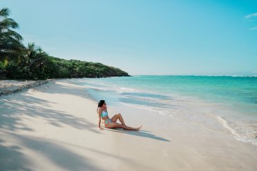 Woman sitting on the white sand at Flamenco Beach in Culebra, looking out at the calm turquoise water under a clear Caribbean sky.