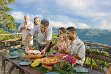 Chef serves a colorful puerto rican dish to a group at a scenic outdoor table, surrounded by mountains and greenery from Cayey, Puerto Rico.