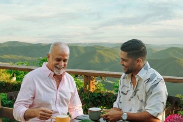 Two men enjoying coffee at Hacienda Siempreviva in Cayey, Puerto Rico, with mountain views in the background.