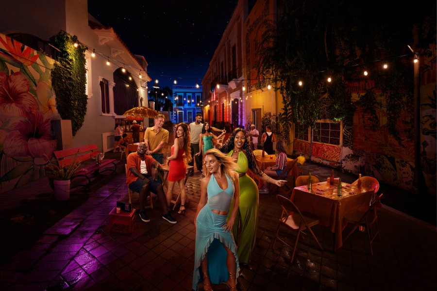 Cast members from TLC’s 90 Day: Hunt for Love pose on a colorful, mural-lined street in Puerto Rico at night, surrounded by café tables and string lights.