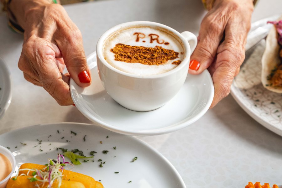 A cup of Puerto Rican coffee topped with cinnamon sits beside fried bites during a food stop in Lares.