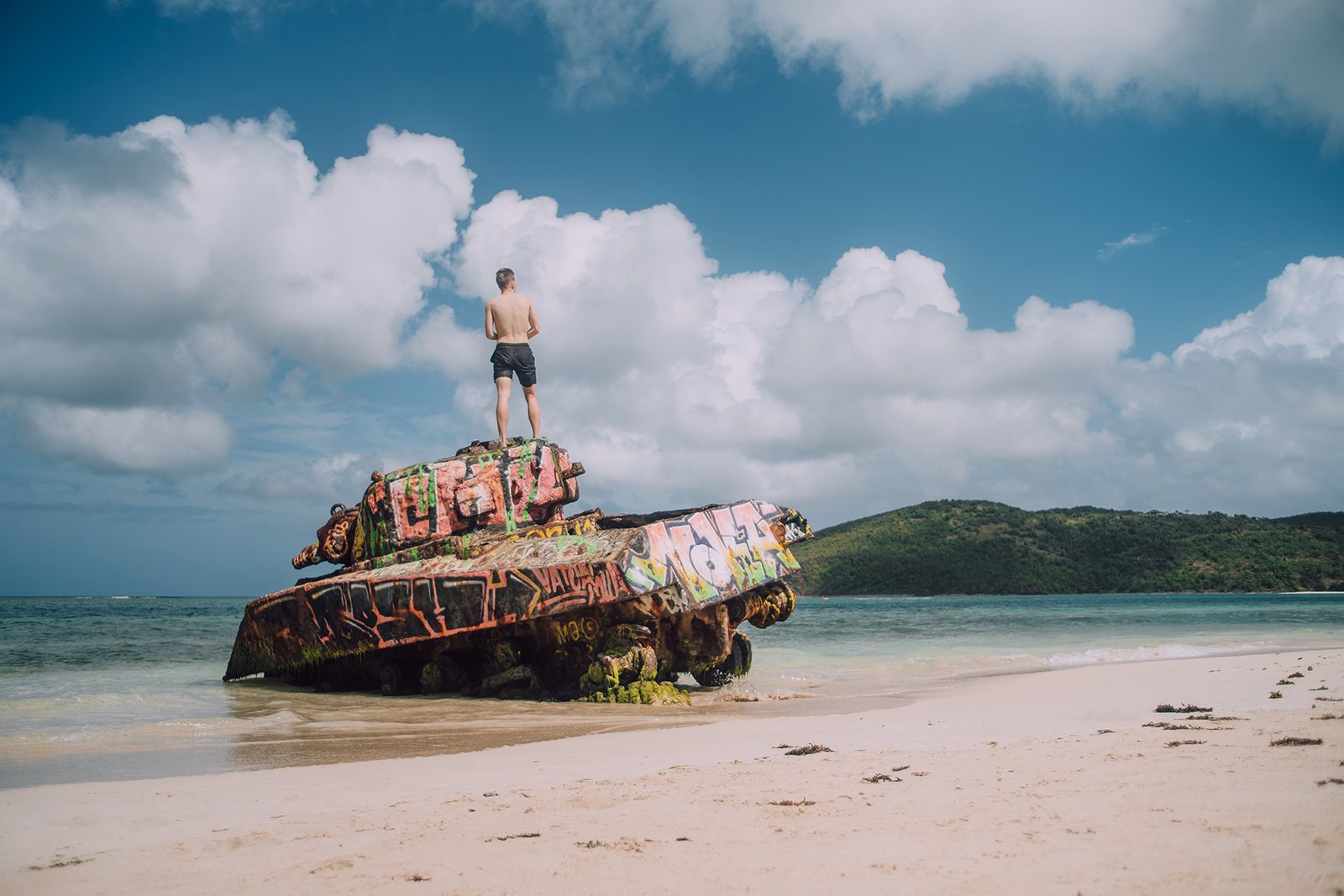 A man stands at the top of an abandoned war tank in Flamenco Beach