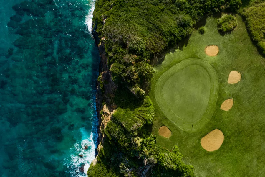 A golf green alongside a cliff on the ocean.