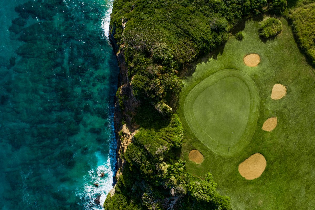 A golf green alongside a cliff on the ocean.