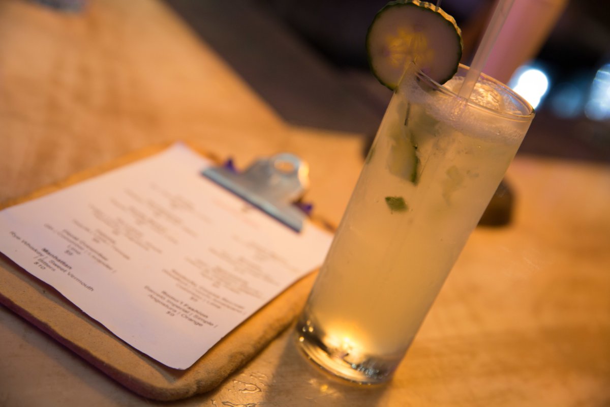 A highball cocktail next to a menu on a clipboard sitting on a table.