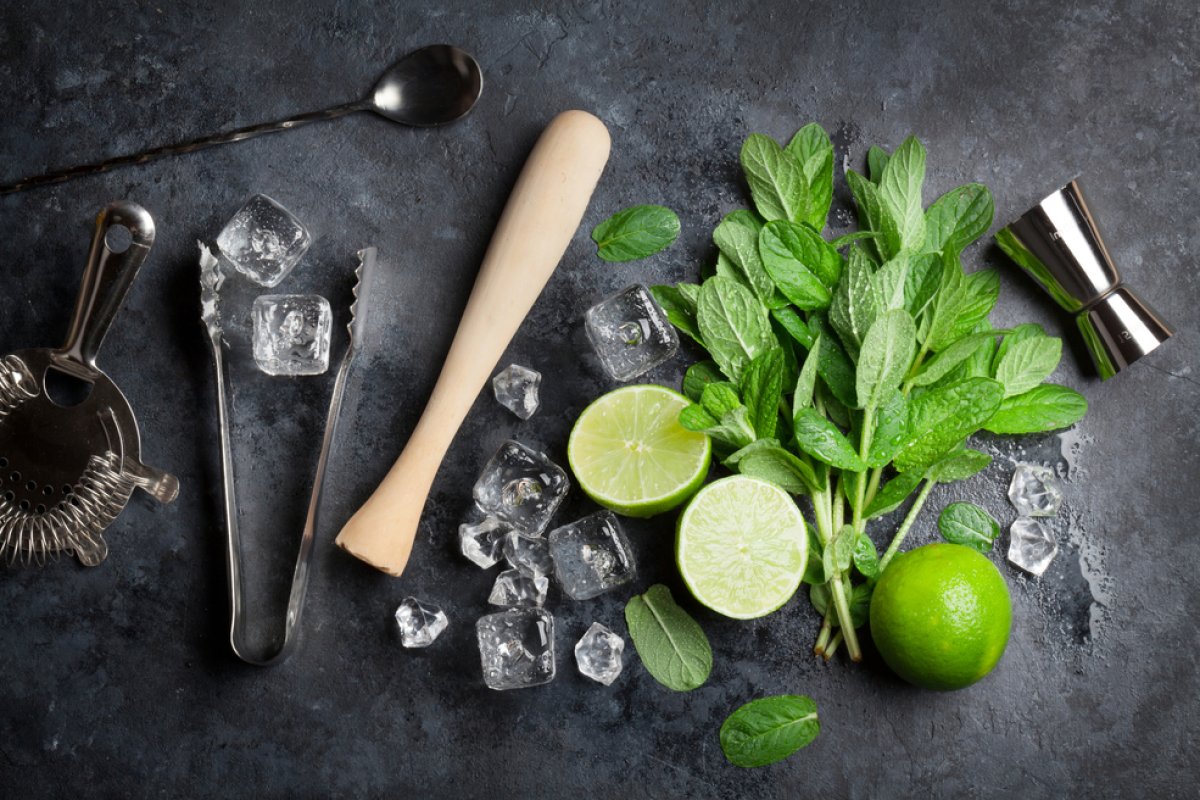 A display of mint leaves, limes, and cocktail tools for making mojitos.