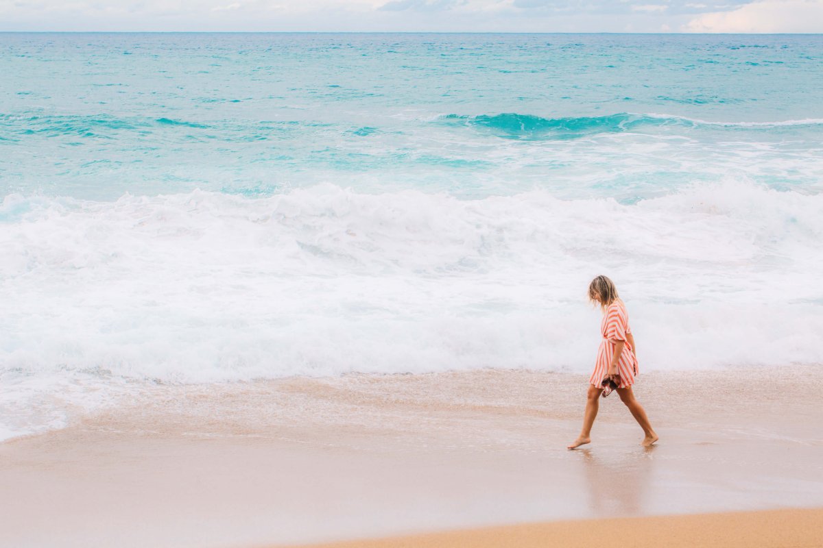 woman walking along the sand with her feet in aquamarine waves. 