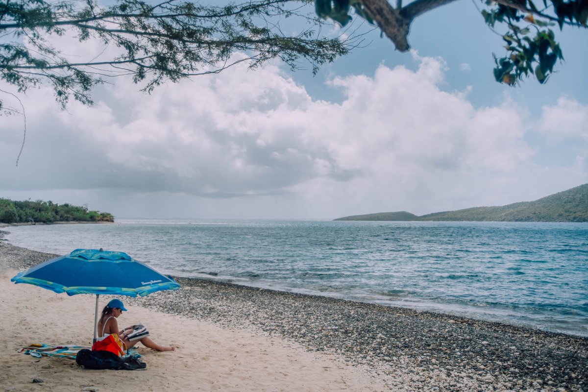 Woman relaxing under a blue umbrella on Tamarindo Beach in Culebra. 