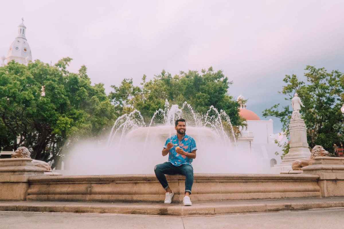 Hombre sonriendo junto a una fuente en Plaza Las Delicas en Ponce.