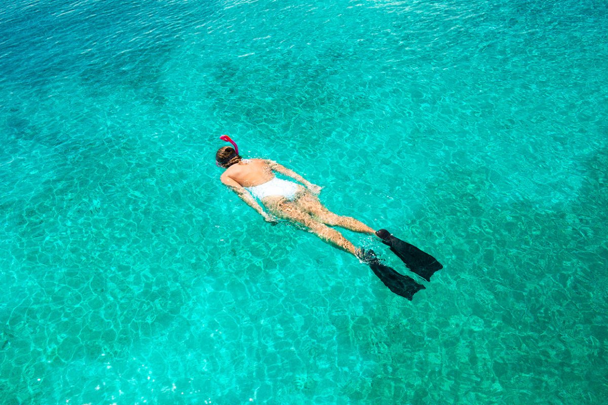 Mujer buceando en traje de baño blanco contra aguas turquesas.
