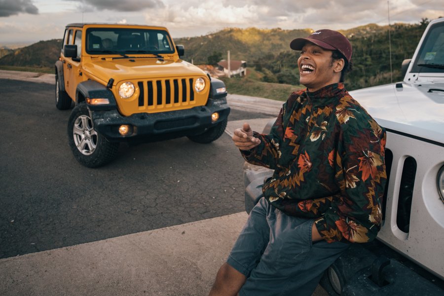 A smiling guy leans against the front of a car