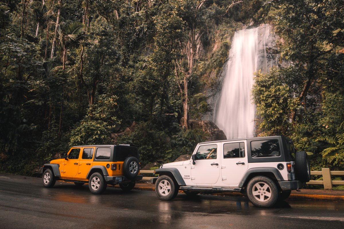 Two jeeps are parked in front of a waterfall