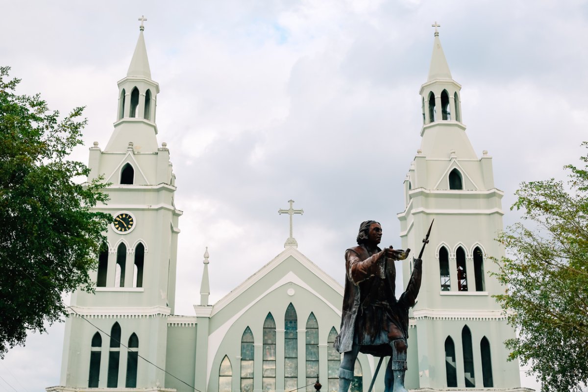 Altísimas torres de iglesia blancas en el fondo y una estatua de bronce de Colón en primer plano