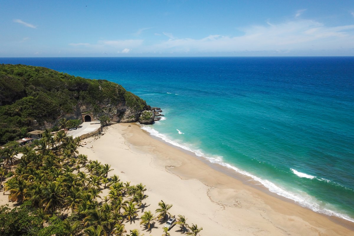 An aerial view of the Tunel de Guajataca adjacent to a white sand beach and turquoise sea.