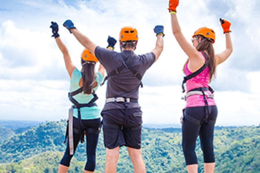 Three people with hands in the air wearing zipline gear.