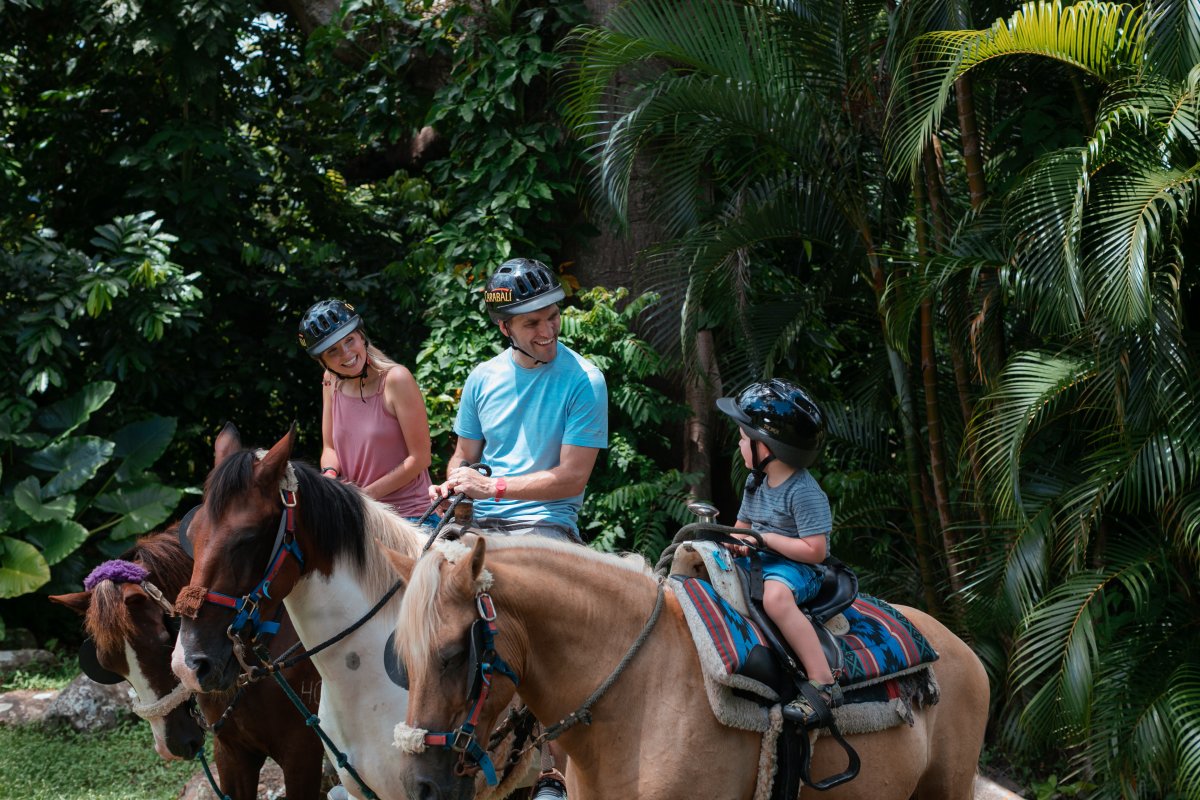 Una familia de tres personas sentada sobre tres caballos en un espacio verde al aire libre.