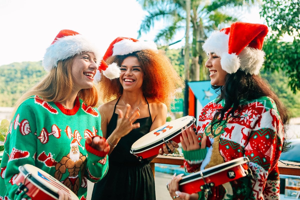 Three young ladies wearing Santa hats and Christmas sweaters playing the pandero, a typical instrument of Puerto Rico's Christmas parrandas.