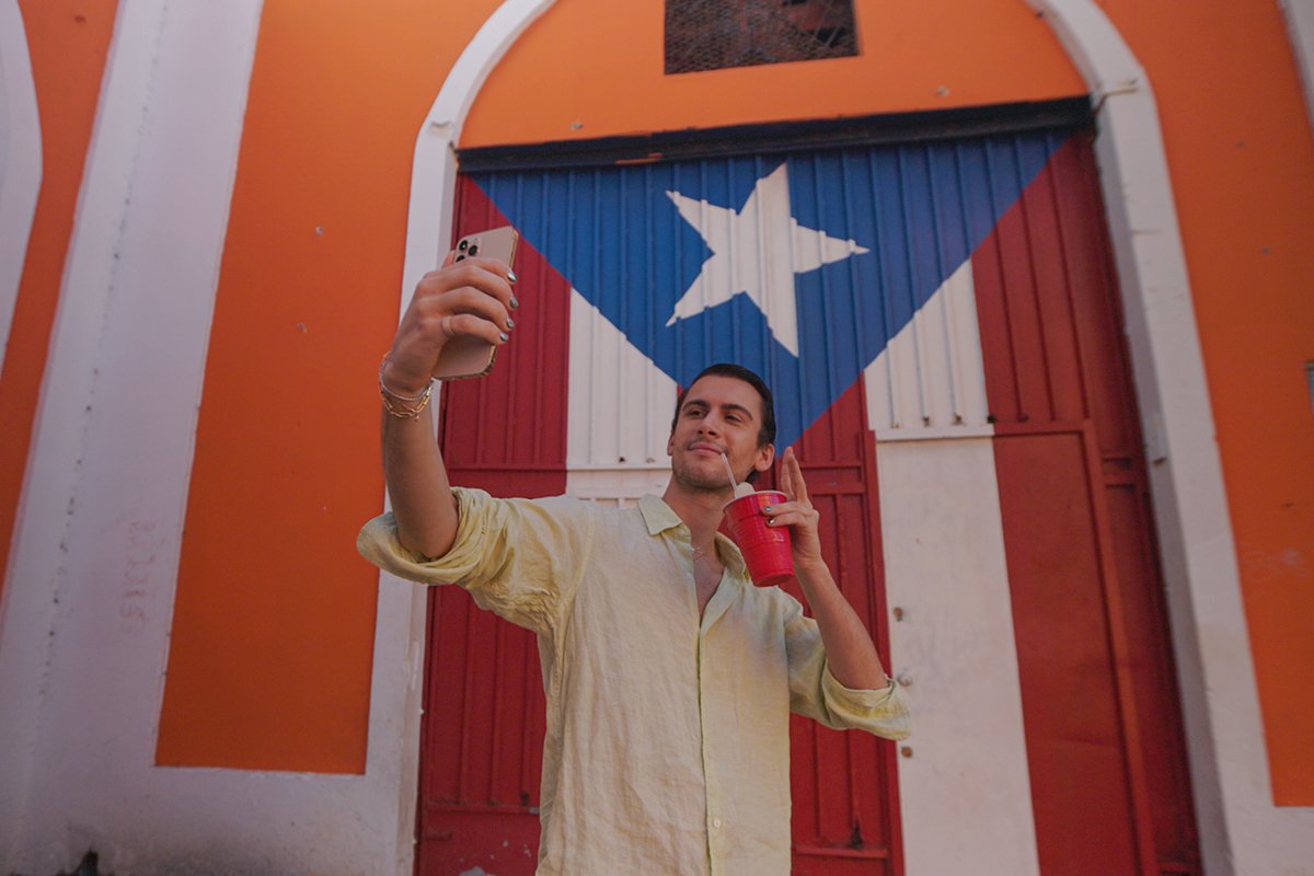 Fashion designer Christian Cowan poses in front of a Puerto Rican flag on a visit to Puerto Rico.