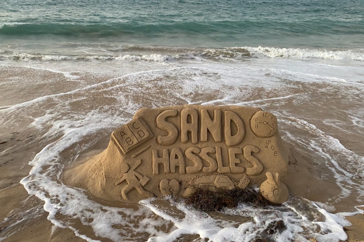 A sand castle with the words Sand Hassles gets lapped by waves on a Puerto Rico beach
