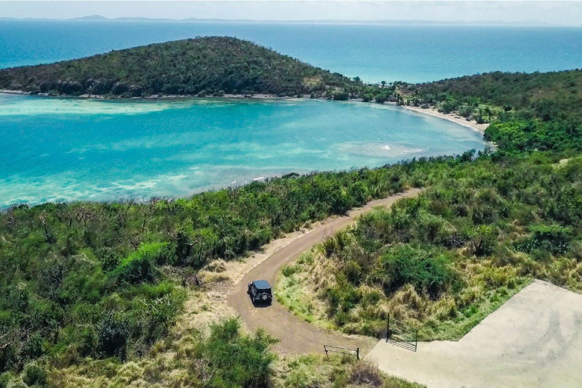 A car drives a winding road near a picturesque beach in Puerto Rico.