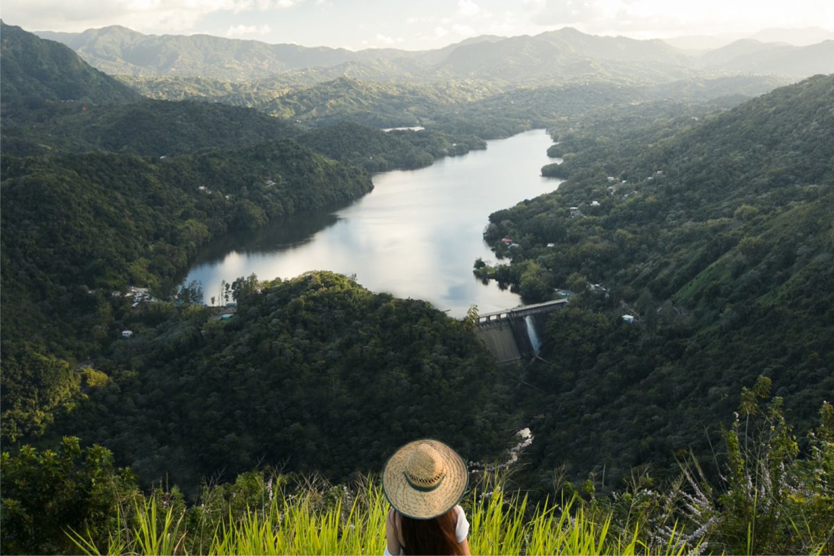 A woman looks out over a beautiful mountain view with a body of water in the distance in Utuado.