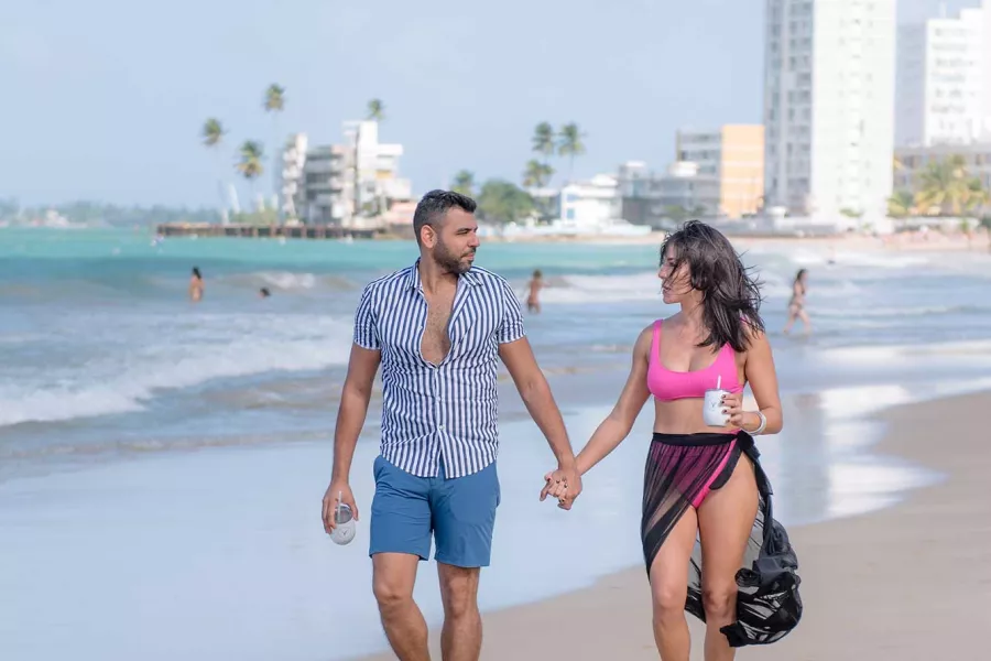 A couple holding hands strolls on a beach near the Hyatt Centric San Juan - Isla Verde.