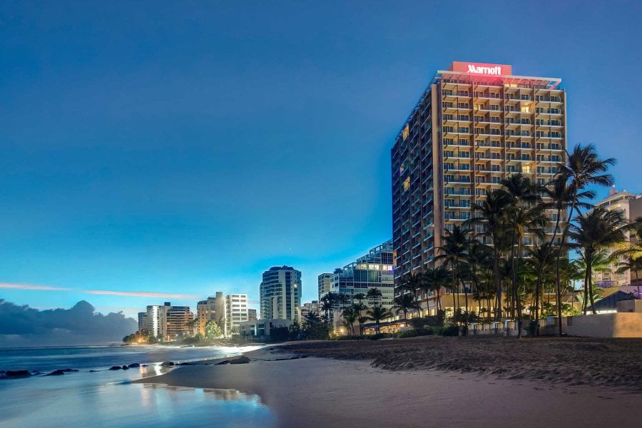 The exterior of the San Juan Marriott Resort & Stellaris Casino, with the word "Marriott" illuminated, with the beach in the foreground and the night sky behind it.