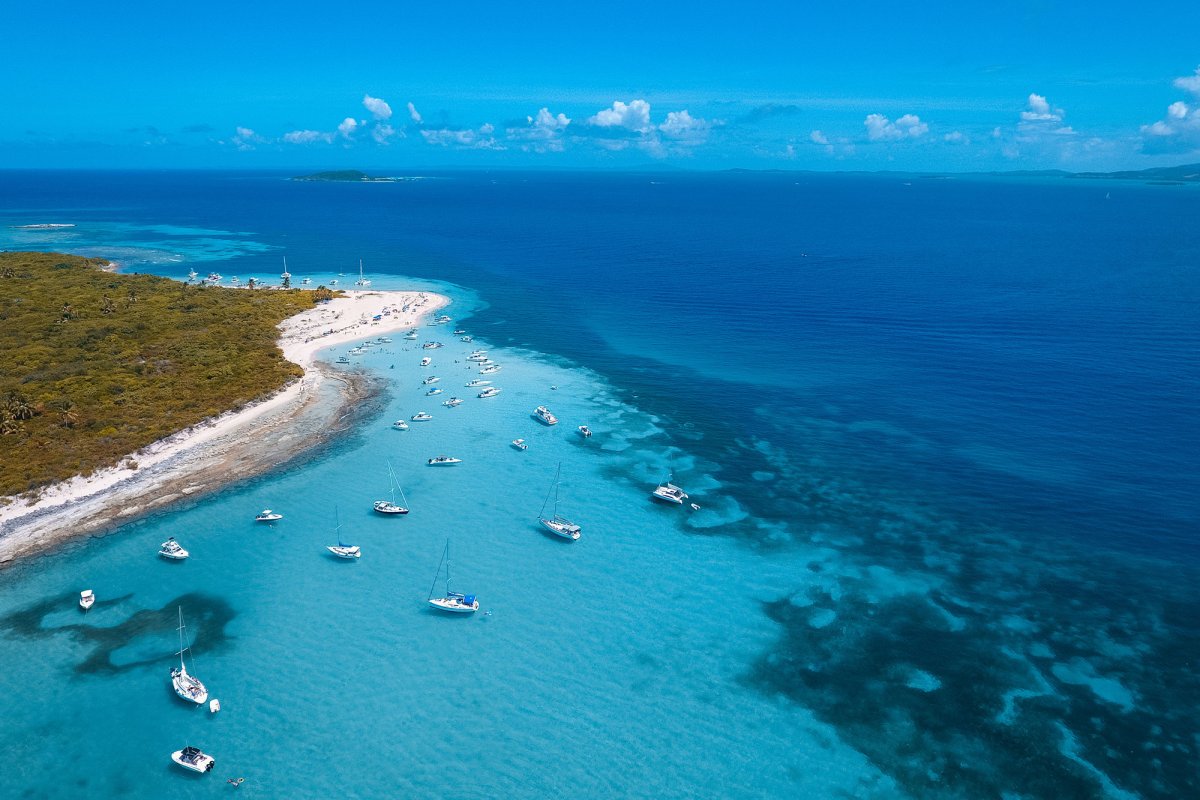 Overhead view of the coastline of Cayo Icacos on the east coast of Puerto Rico, with clear-blue water and several boats anchored near the shore.