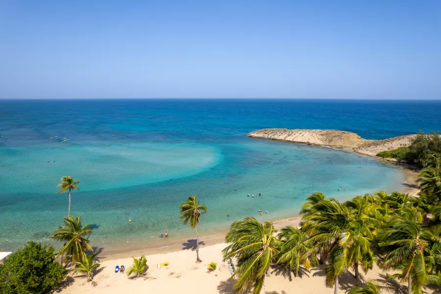 Aerial view of Montones Beach in Isabela. Quiet beach with clear, shallow water and a natural rock barrier creating a calm swimming area. 