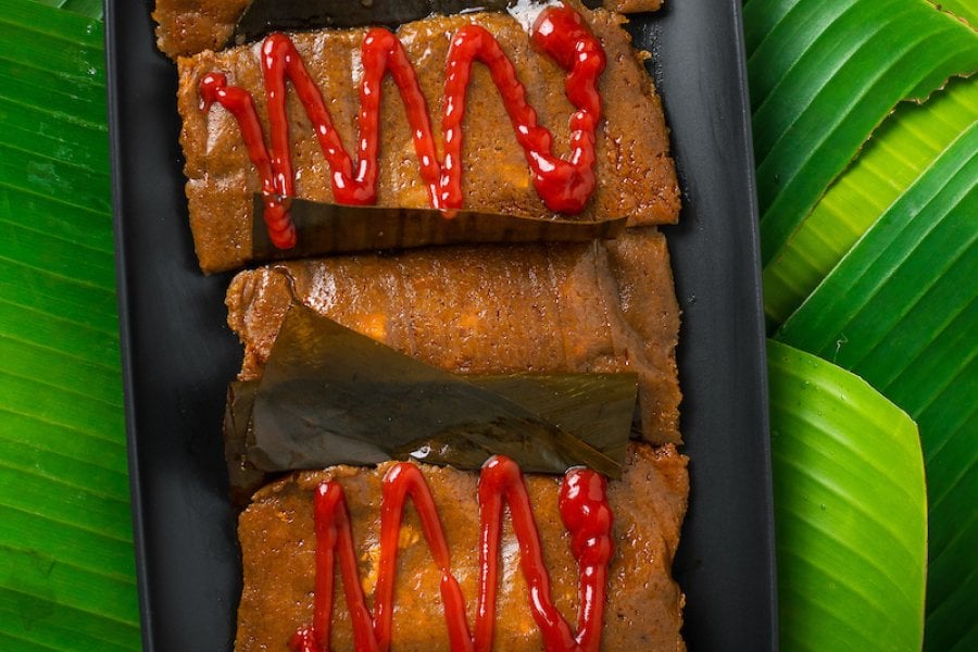 Plate of pasteles with and without ketchup on top of banana leaves.