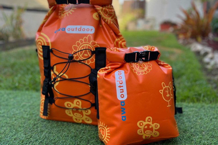 Two dry bags in the bright orange shade of Puerto Rico Sunshine sit on display atop green grass.