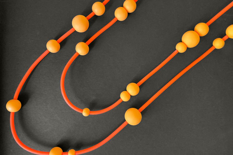Overhead shot of a beaded necklace by Knot Predictable in shades of orange on a black background.