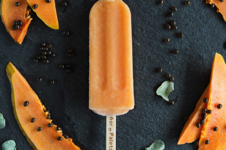 An orange popsicle is pictured on a black background surrounded by orange fruit slices.