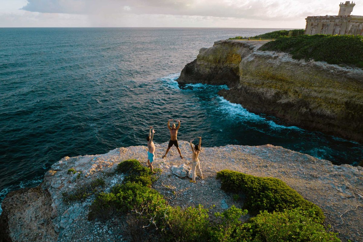 Three people practice yoga on an oceanside cliff during a retreat at Finca Victoria. Vieques, Puerto Rico.