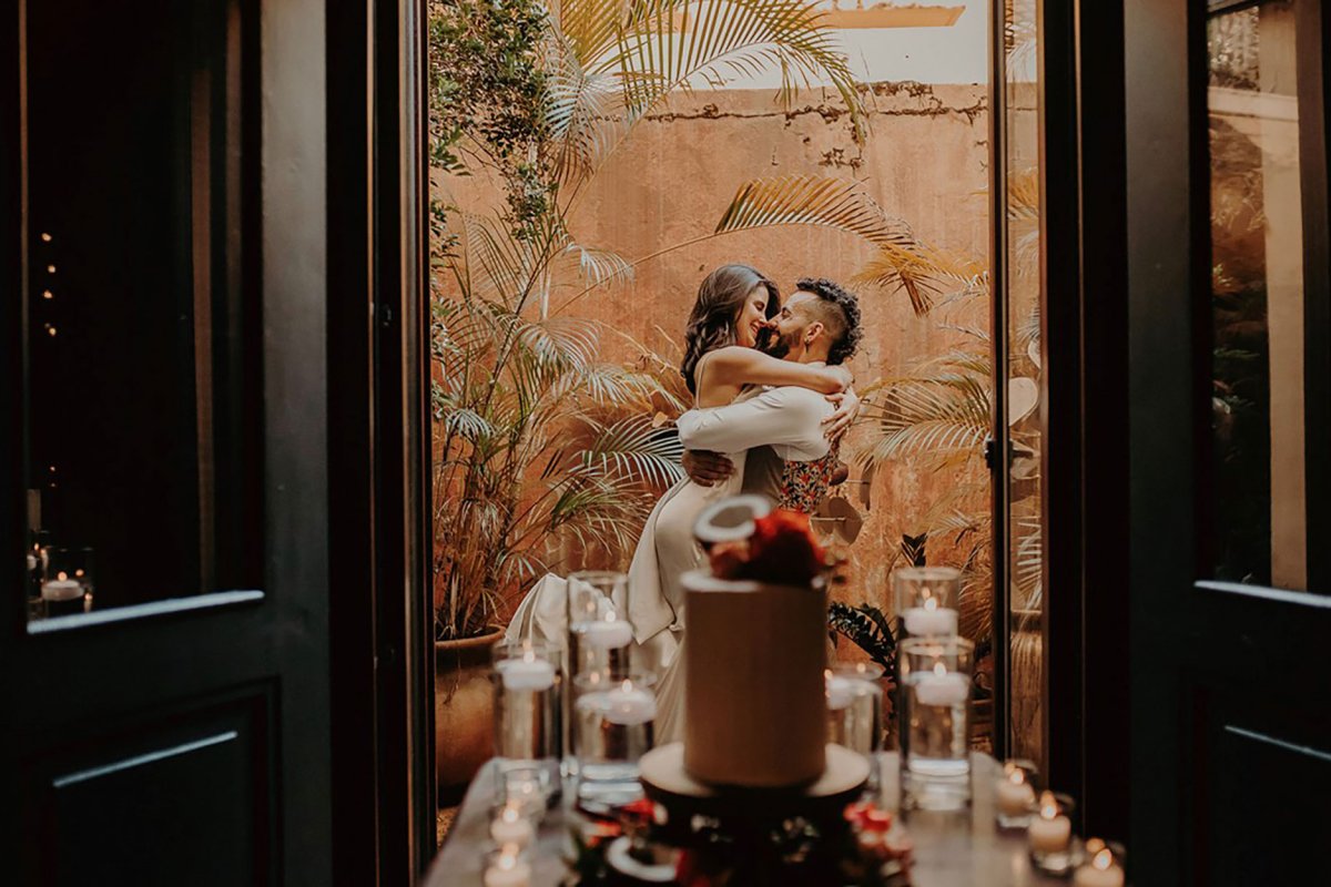 A couple embraces on a balcony with a wedding cake in the foreground at El Convento in San Juan, Puerto Rico.