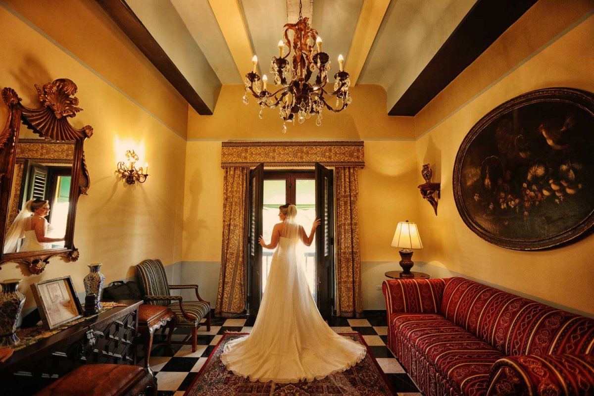 A bride, pictured from behind, opens a large historic window at Hotel El Convento in Old San Juan, Puerto Rico. Photo by Noel Pilar.