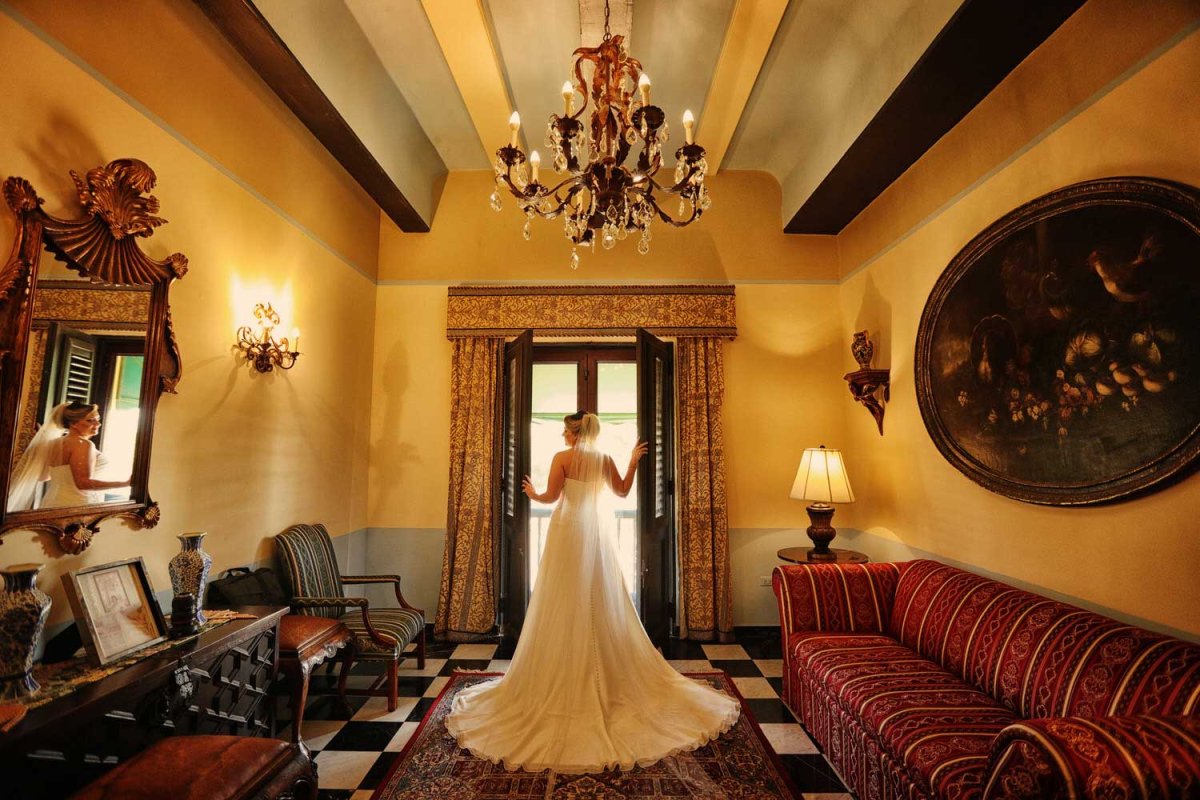 Una novia, fotografiada desde atrás, abre una gran ventana histórica en el Hotel El Convento en el Viejo San Juan, Puerto Rico. Foto de Noel Pilar.