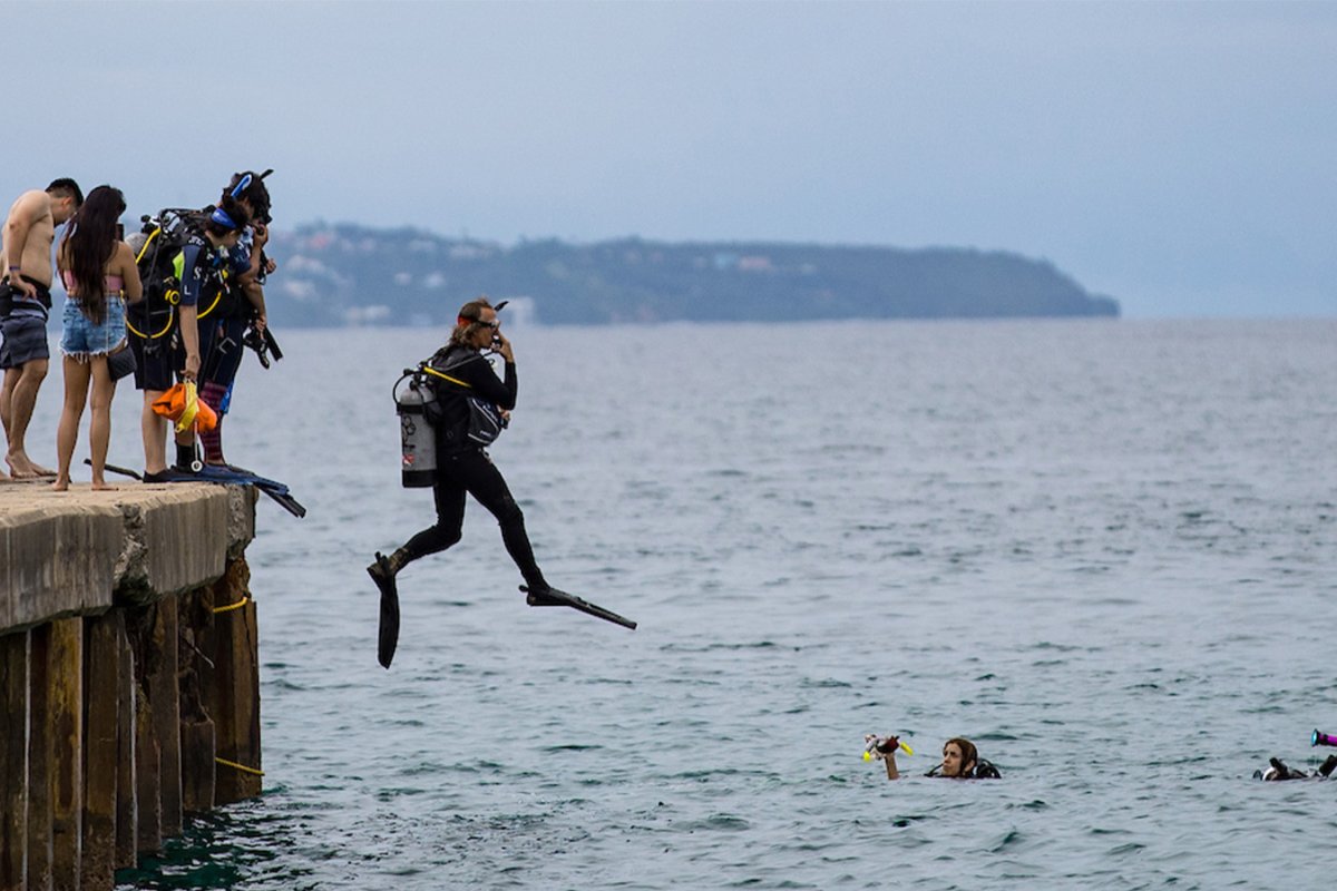 A dozen teens and adults jumping into the open water in Aguadilla, Puerto Rico for a scuba diving lesson.